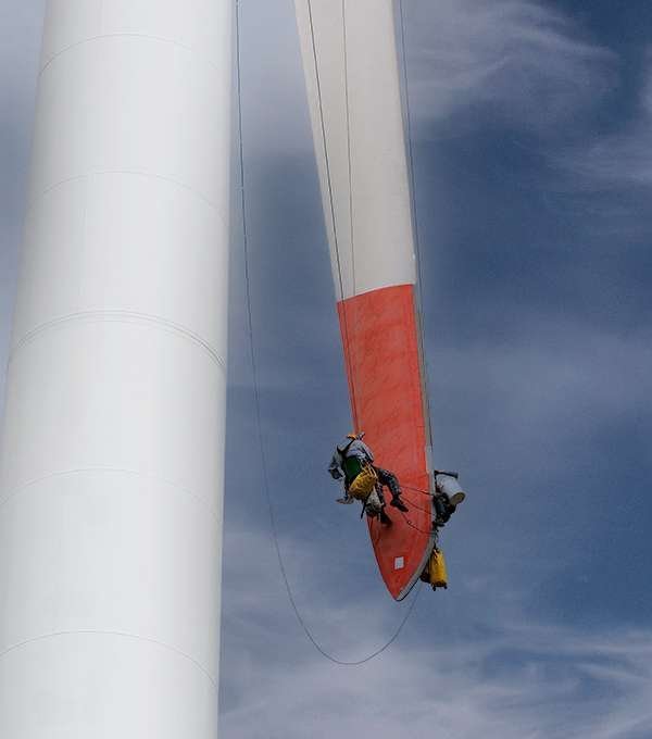 Técnicos trabajando en suspensión sobre el aspa de un aerogenerador
