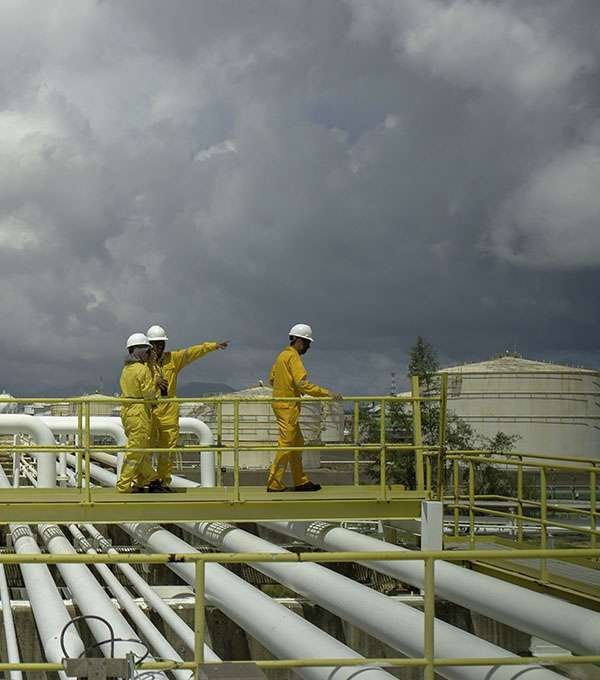 Personal con equipo de protección sobre racks de tubería en una planta petroquímica bajo cielo tormentoso