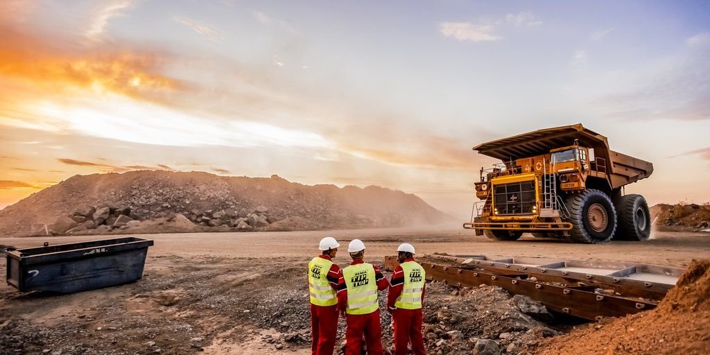 Cuadrilla de trabajadores con casco y chaleco reflectante junto a un camión minero al atardecer
